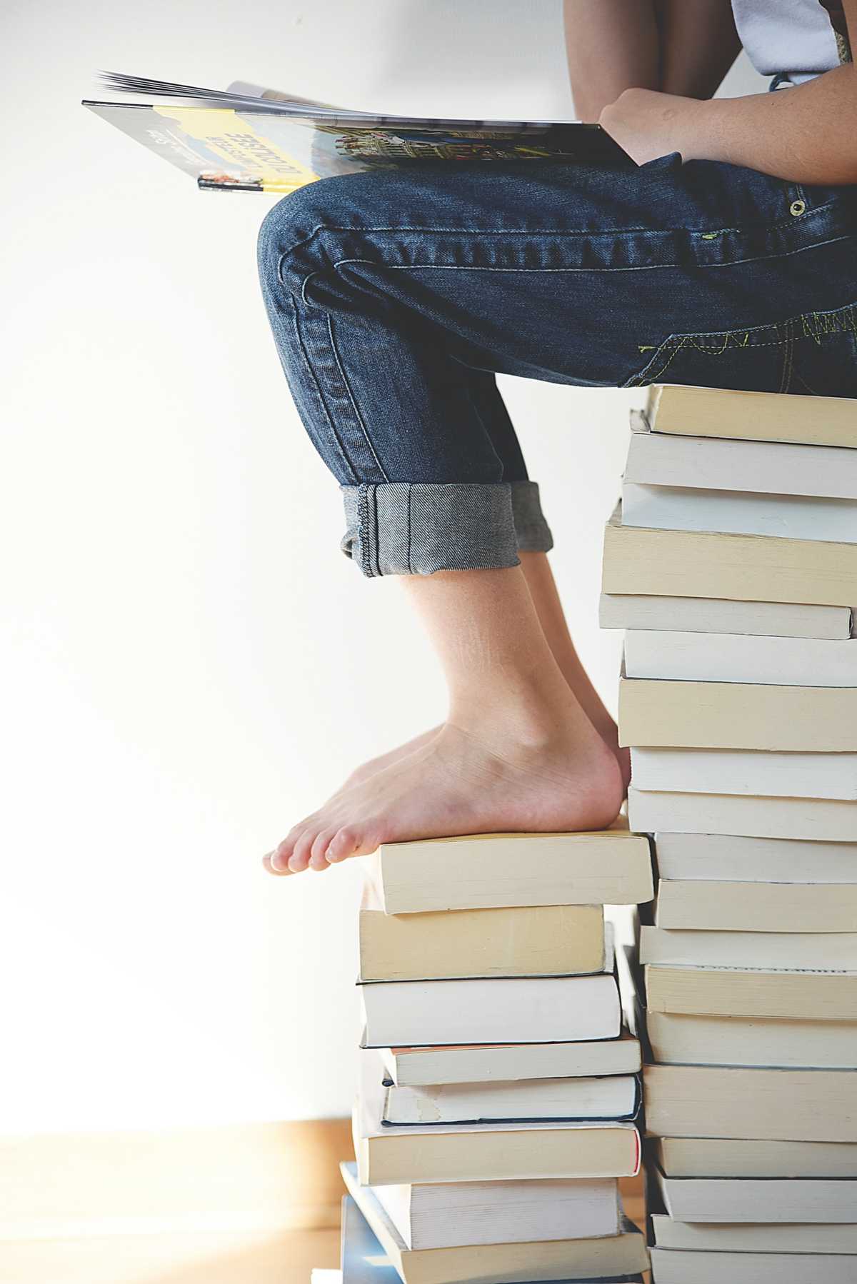 A seated child reading on a stack of books.